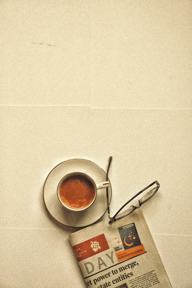 A cup of coffee beside glasses and a newspaper on a sunlit table